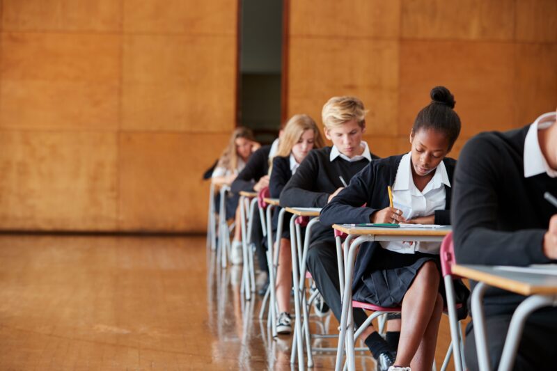 Teenage,Students,In,Uniform,Sitting,Examination,In,School,Hall